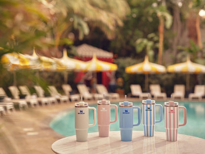 Set of colorful tumblers on a table by a poolside with lounge chairs and umbrellas in the background.