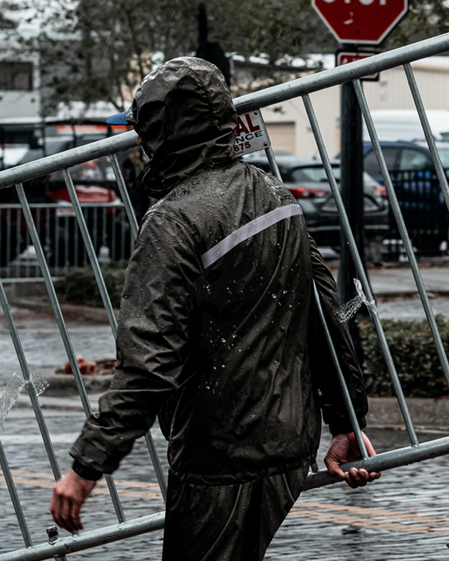 Person wearing a waterproof raincoat walking through a rainy street carrying metal equipment