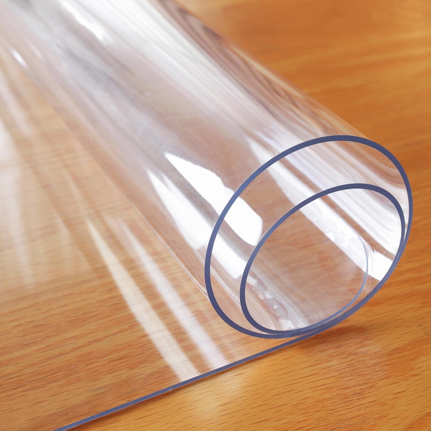 OstepDecor clear table protector rolled up on a wooden surface showing its thick, flexible plastic material and clear transparency.