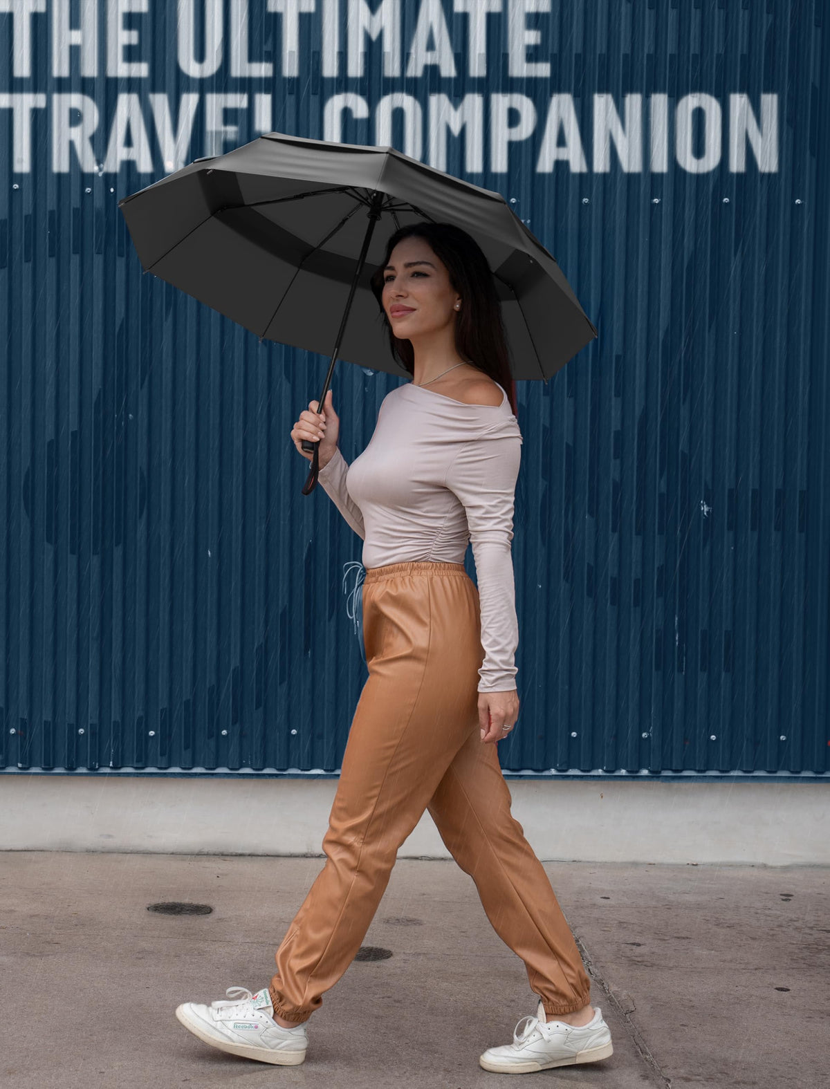 Woman holding an open black Repel Windproof Travel Umbrella against a blue textured backdrop with "The Ultimate Travel Companion" text overlay.