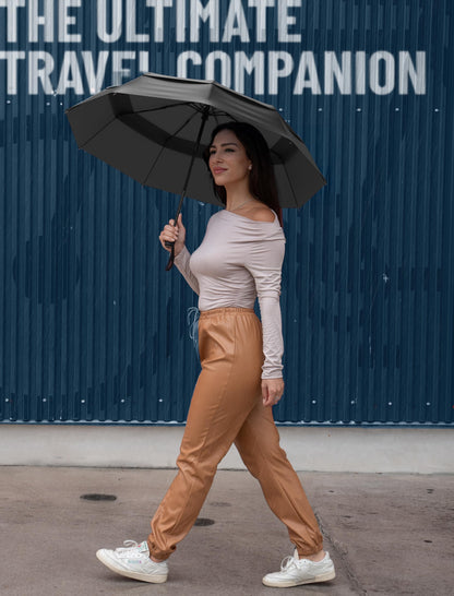 Woman holding an open black Repel Windproof Travel Umbrella against a blue textured backdrop with "The Ultimate Travel Companion" text overlay.