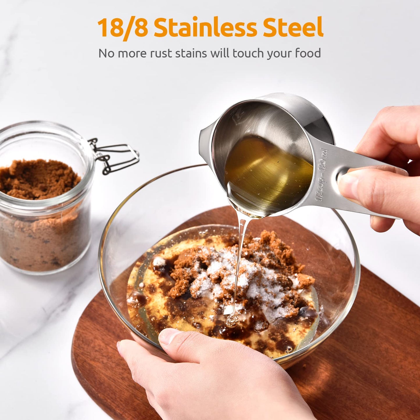 Stainless steel measuring cup being used to pour liquid into a dish with food, on a white background.
