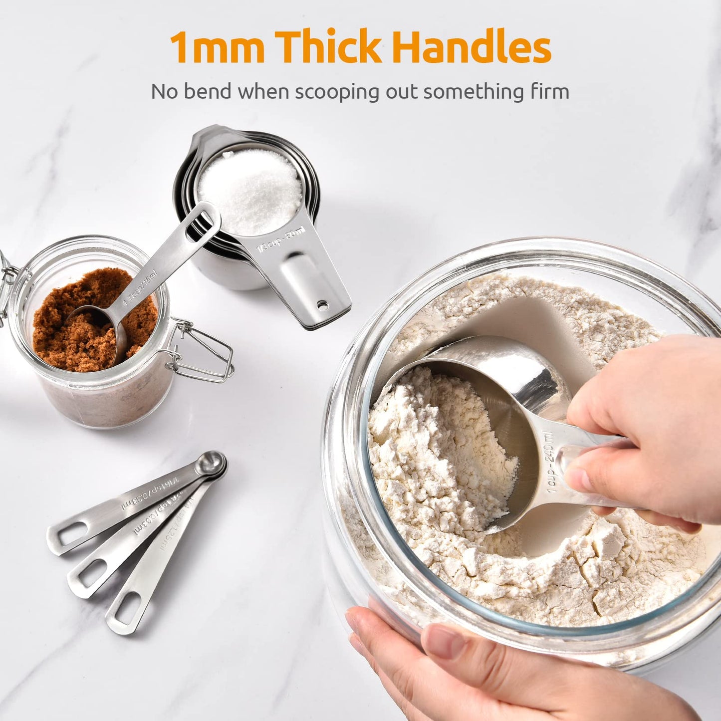 Metal measuring spoons and cups being used to measure flour on a white surface.